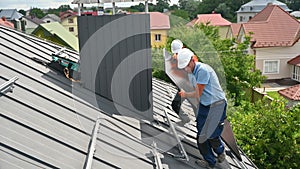 Workers building solar panel system on roof of house. Installers carrying photovoltaic solar module