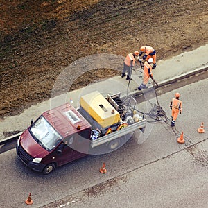 Workers with car and a hipping hammer take off the asphalt on the road, top view