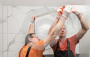 Workers are connecting the glass walls of the shower with a metal bar