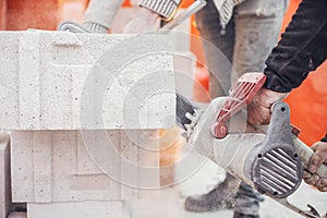 Workers cutting autoclaved aerated concrete block with chainsaw closeup. Builders cutting white blocks for masonry installation.