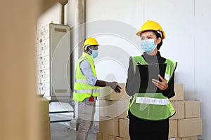 Workers from different ethinic wearing facial mask and safety vest working in warehouse checking for the inventory using tablet