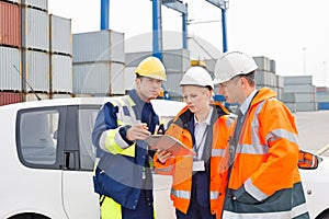 Workers discussing over clipboard beside car in shipping yard