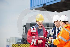 Workers discussing over clipboard in shipping yard