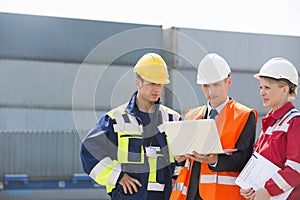 Workers discussing over laptop in shipping yard