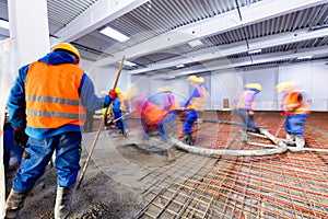 Workers do concrete screed on floor with heating in a new warehouse building