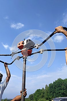 Workers are drilling pits for poles, starting work with a hand drill, drilling the ground