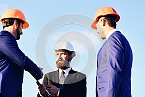 Workers and engineer hold meeting on sky background.