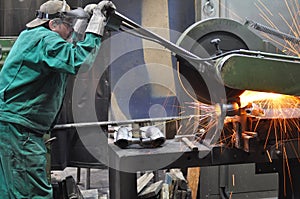 Workers in a foundry grind castings with a grinding machine - He