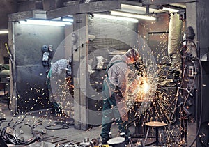 Workers in a foundry grind castings with a grinding machine - He