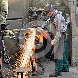 Workers in a foundry grind castings with a grinding machine - He