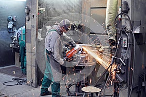 Workers in a foundry grind castings with a grinding machine - He