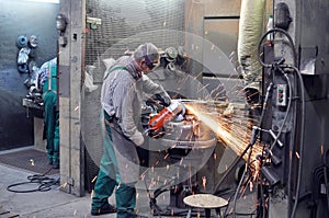 Workers in a foundry grind castings with a grinding machine - He photo