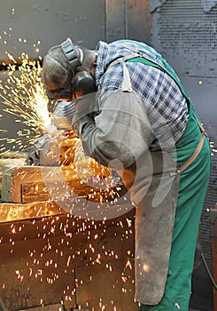 Workers in a foundry grind castings with a grinding machine - He