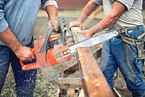 Workers, handymen cutting timber wood using mechanical chainsaw.