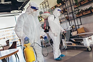 Workers in hazmat suits disinfecting indoor of cafe or restaurant, pandemic health risk, coronavirus