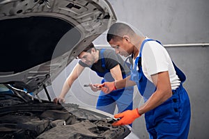 Workers inspecting the hood and engine of a car