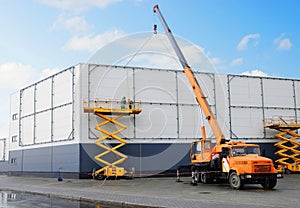 Workers install big billboard on the unfinished building supermarket. Construction crane