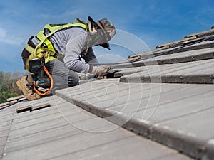 Workers are installing gray roof tiles wearing seat belts to ensure safe working at heights