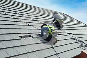 Workers are installing gray roof tiles wearing seat belts to ensure safe working at heights