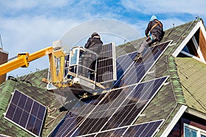 Workers installing solar panels on private home hexagonal roof felt on sunny day  blue sky.