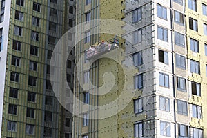 workers are insulating the wall of a building. Construction site. Foreign workers. Insulation panels. Hanging cradle