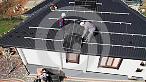 Workers lifting up photovoltaic solar module while installing solar panel system on roof of house.