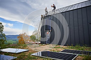 Workers lifting up photovoltaic solar module while installing solar panel system on roof of house.