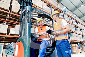 Workers in logistics warehouse at forklift checking list