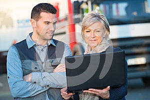 Workers looking at laptop stood outdoors in front lorry