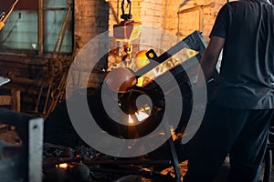 Workers at metallurgical plant pour molten metal from furnace into foundry ladle
