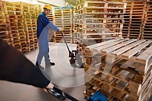 Workers moving wooden pallets with manual forklift in warehouse