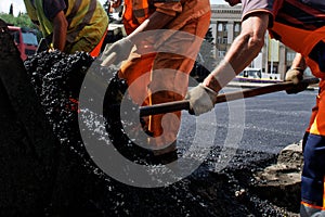 Workers in orange uniform are laying hot asphalt on a city street. Road repair