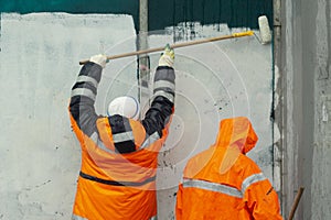 Workers paint wall. Wall flogging. Orange clothing of workers. Smearing graffiti photo