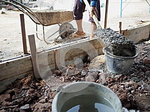 Workers pouring mixed concrete to bucket in construction site.