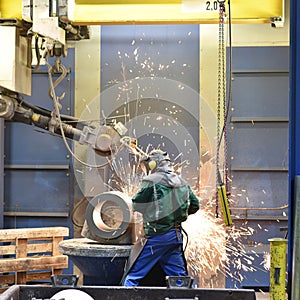 Workers in protective equipment in a foundry work on a casting with a grinding machine at the workplace