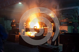 Workers in protective gear operate in a foundry, handling molten metal with machinery. Industrial manufacturing process