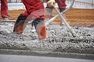 Workers in red boots with rake leveled the concrete