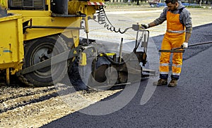 Workers regulate tracked paver laying asphalt