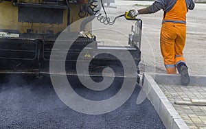 Workers regulate tracked paver laying asphalt heated