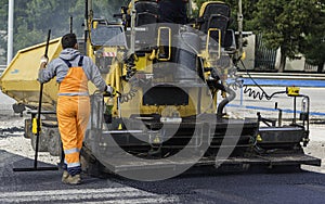 Workers regulate tracked paver laying asphalt heated