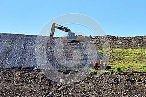 Workers strengthen the soil on the hillside. Flooring on the ground in an old landfill. Excavator works on the hill dump