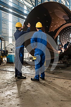 Workers supervising the manufacture of a metallic cylinder