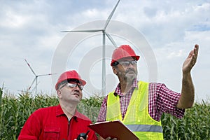 Workers Talking by Wind Turbines in Rural Landscape