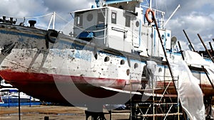 Workers tear off paint on metal in repairs process at shipyard.