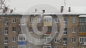 Workers throw white snow from the roof of a multi-storey building. Heavy seasonal male labor. People work as a shovel