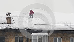 Workers throw white snow from the roof of a multi-story building. Heavy seasonal male labor. People work as a shovel