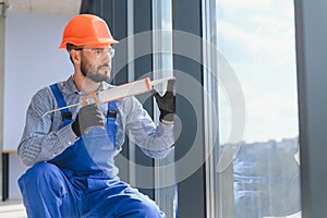 Workers with tube of sealant and suction lifters installing plastic windows indoors.