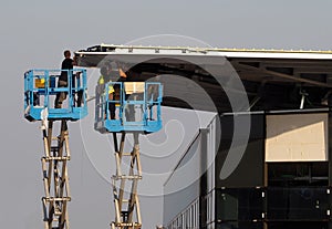 Workers on two cherry pickers, scissor lifts, finish the facade of a new building just build