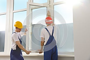 Workers in uniform installing plastic window indoors