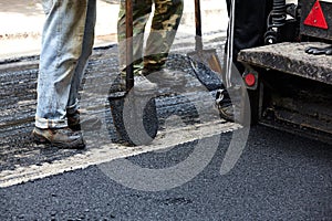 Workers using asphalt paver tools during road construction.